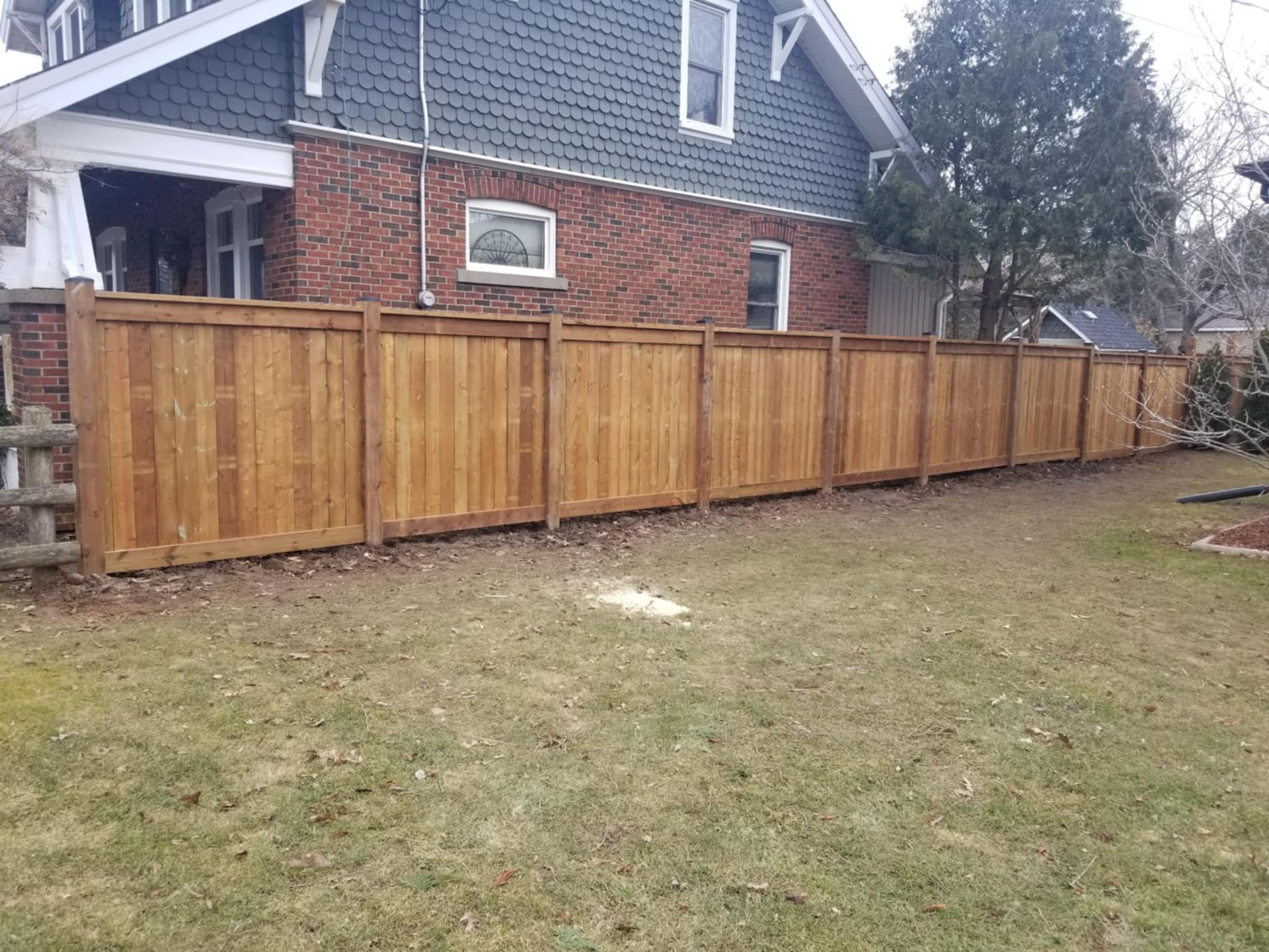 Wooden fence along the side of a brick house with a small grassy lawn.