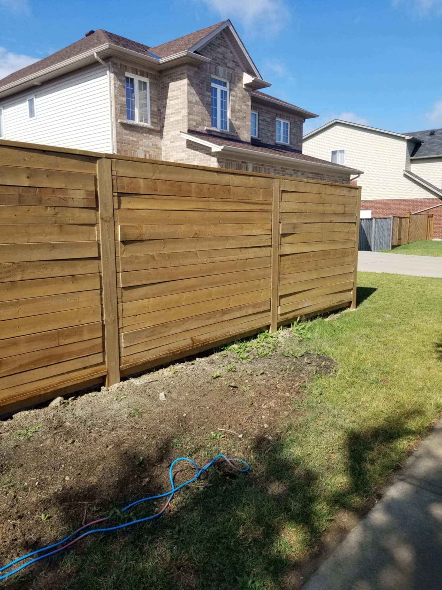 Brown wooden fence in front of a two-story brick house with a grassy lawn.