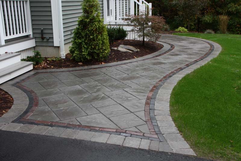 A brick walkway leading to a house with a lush green lawn.