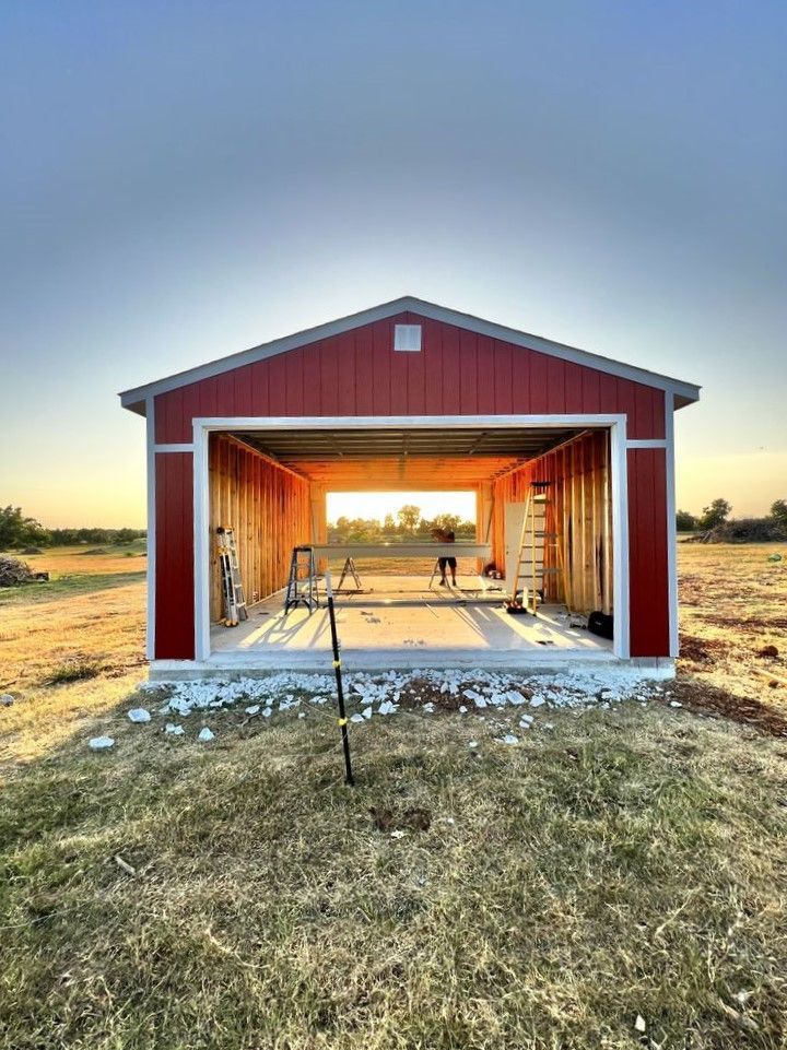 A red garage is being built in a field with the door open.
