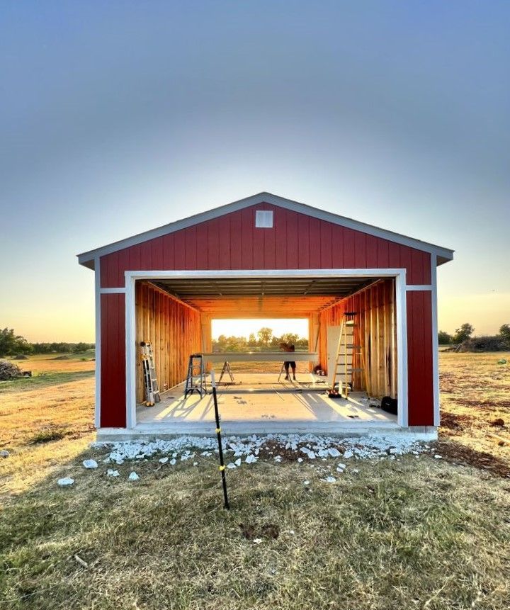 A red garage is being built in a field with the door open.