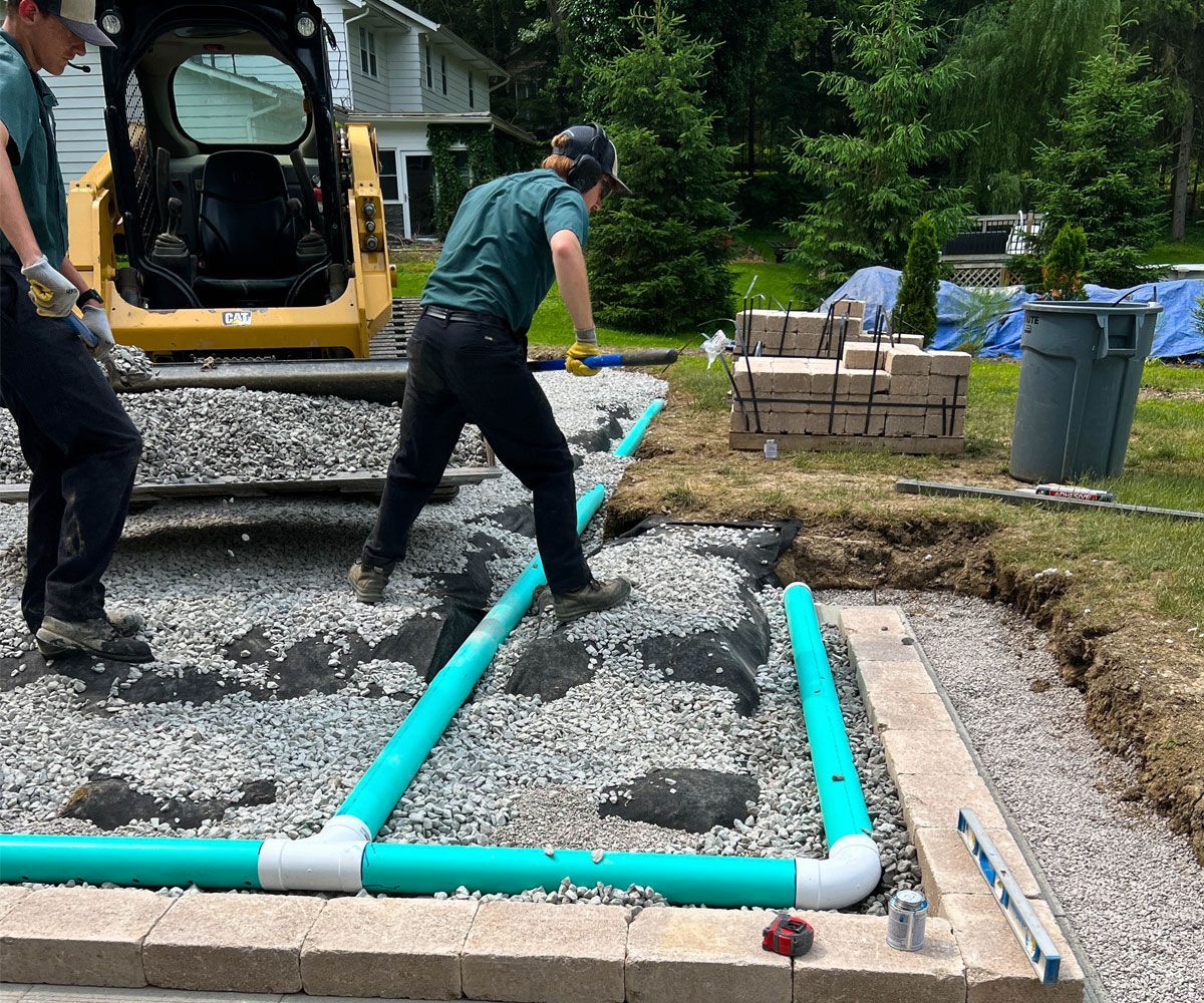 Landscape installation crew installing drainage pipes in a Northeast Ohio backyard so that new paver patio is properly draining.