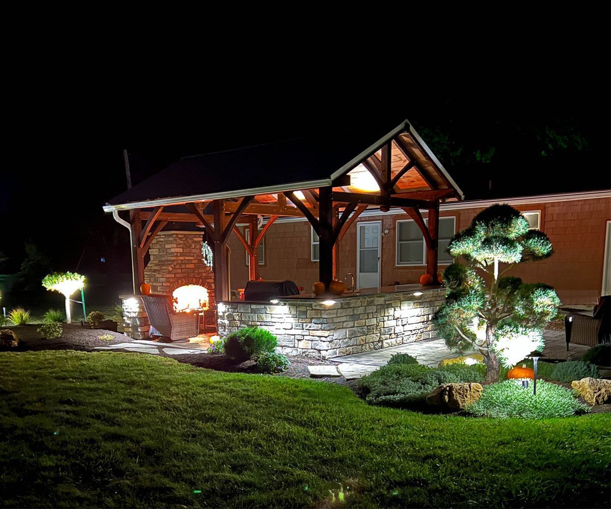 Landscape outdoor lighting in Bath, Ohio backyard patio pavilion with tree uplighting and outdoor kitchen cabinet exterior lighting.