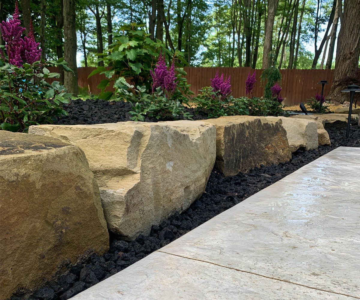 Natural stone outcropping boulders being used as a landscape retaining wall in Bath, Ohio backyard.
