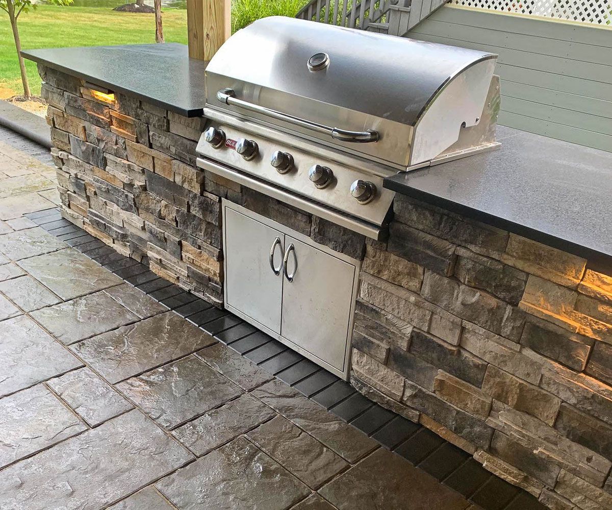 All season outdoor kitchen with louvered roof, built-in high performance gas grill, and stone outdoor cabinetry in Northeast Ohio backyard patio.
