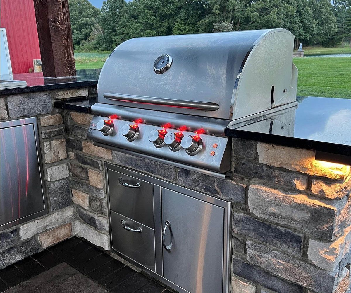 Outdoor living in Summit County with outdoor kitchen, built-in gas grill, and landscape lighting by Chidsey Landscape & Design.