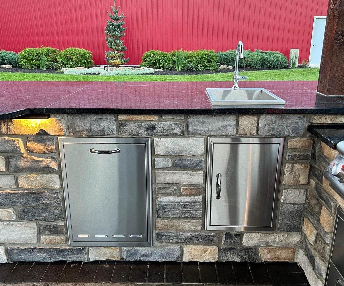 Custom outdoor kitchen cabinets with buil-in sink, outdoor refrigerator, and trash drawer in Copley, Ohio patio by Chidsey Landscape & Design