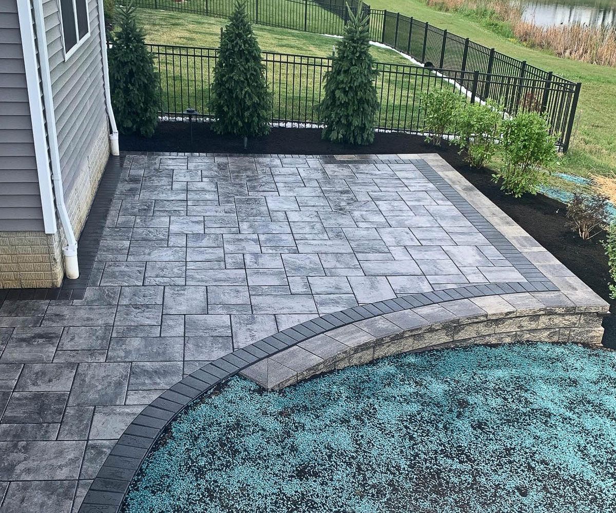 New paver patio with dark paver border and retaining wall on sloped backyard in Copley, OH