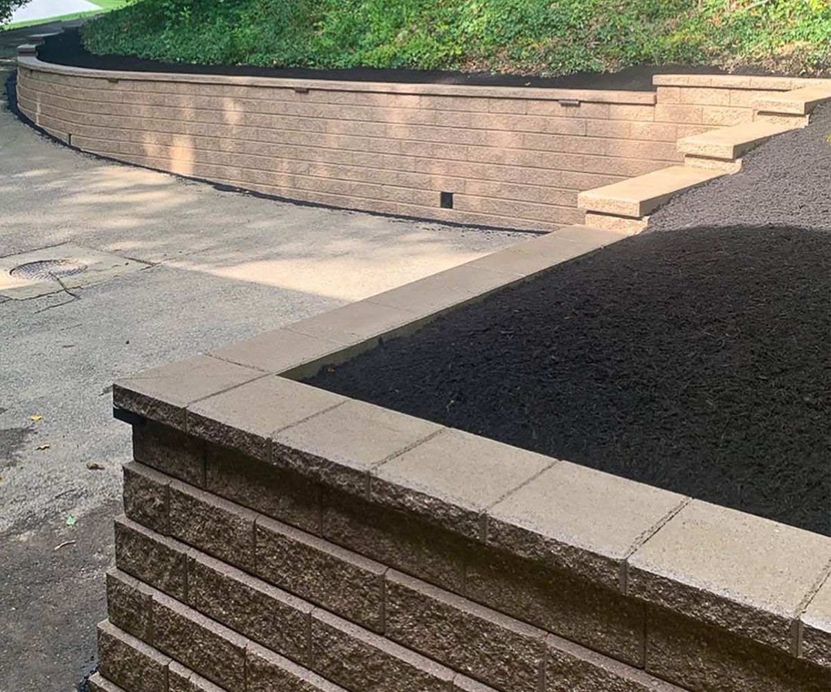 Paving wall block stone retaining wall on sloped front yard by Hudson, OH driveway to help with water runoff and soil erosion.