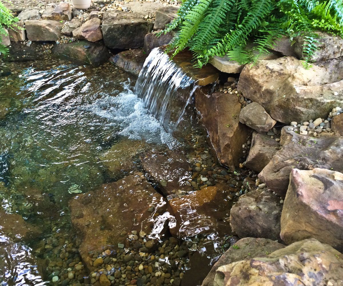 Sheer waterfall in backyard Cuyahoga County Ohio landscape with natural landscape stone boulders, surrounded by lush plantings.