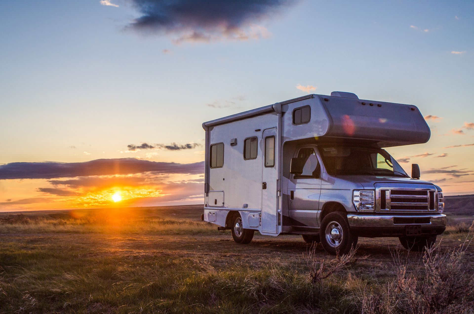 RV parked in a field at sunset, with the sun glowing orange and pink.
