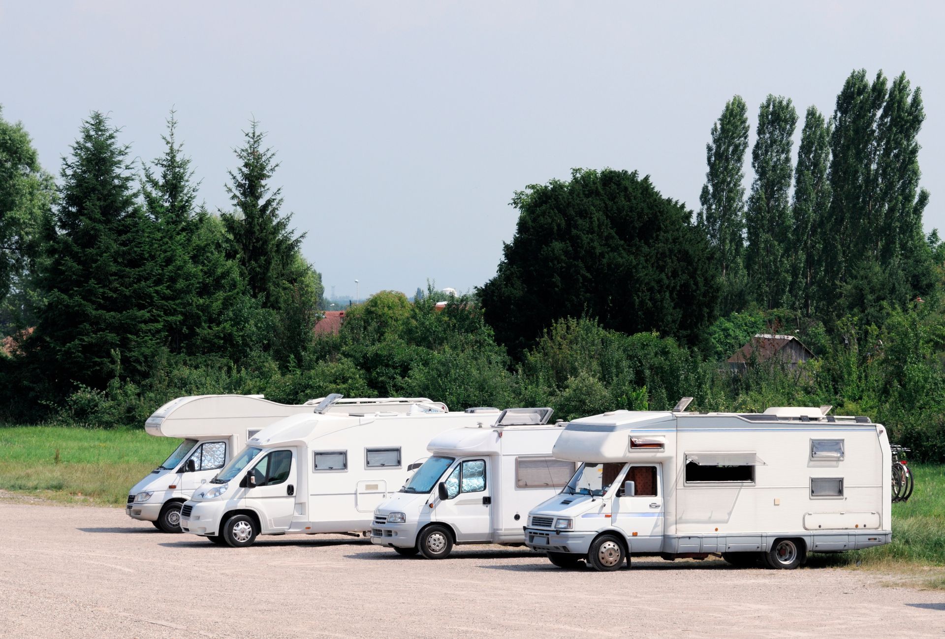 RV parked at a campsite, awning extended, chairs set up; another RV to the right, green grass.