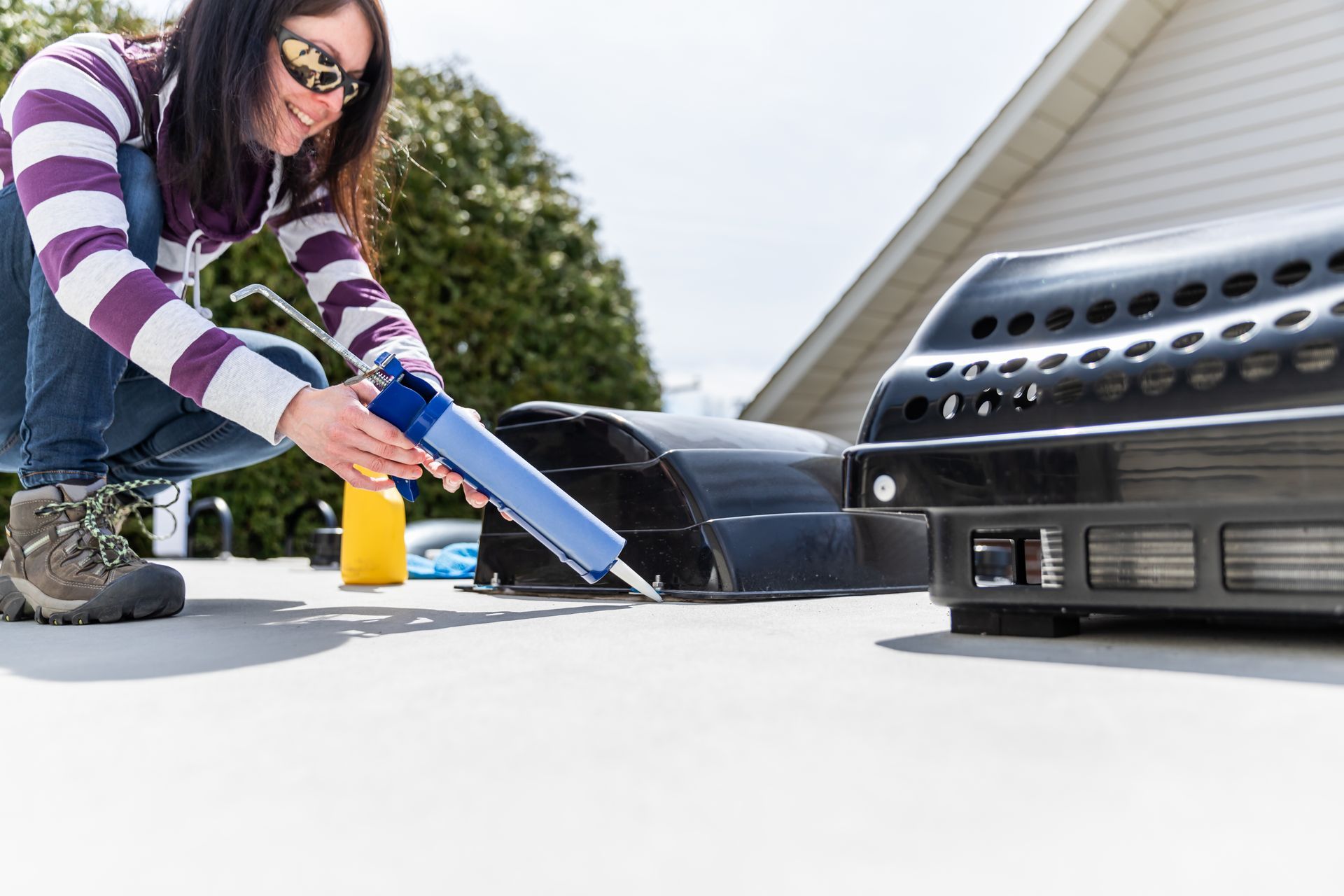 Woman sealing RV roof with caulking gun.