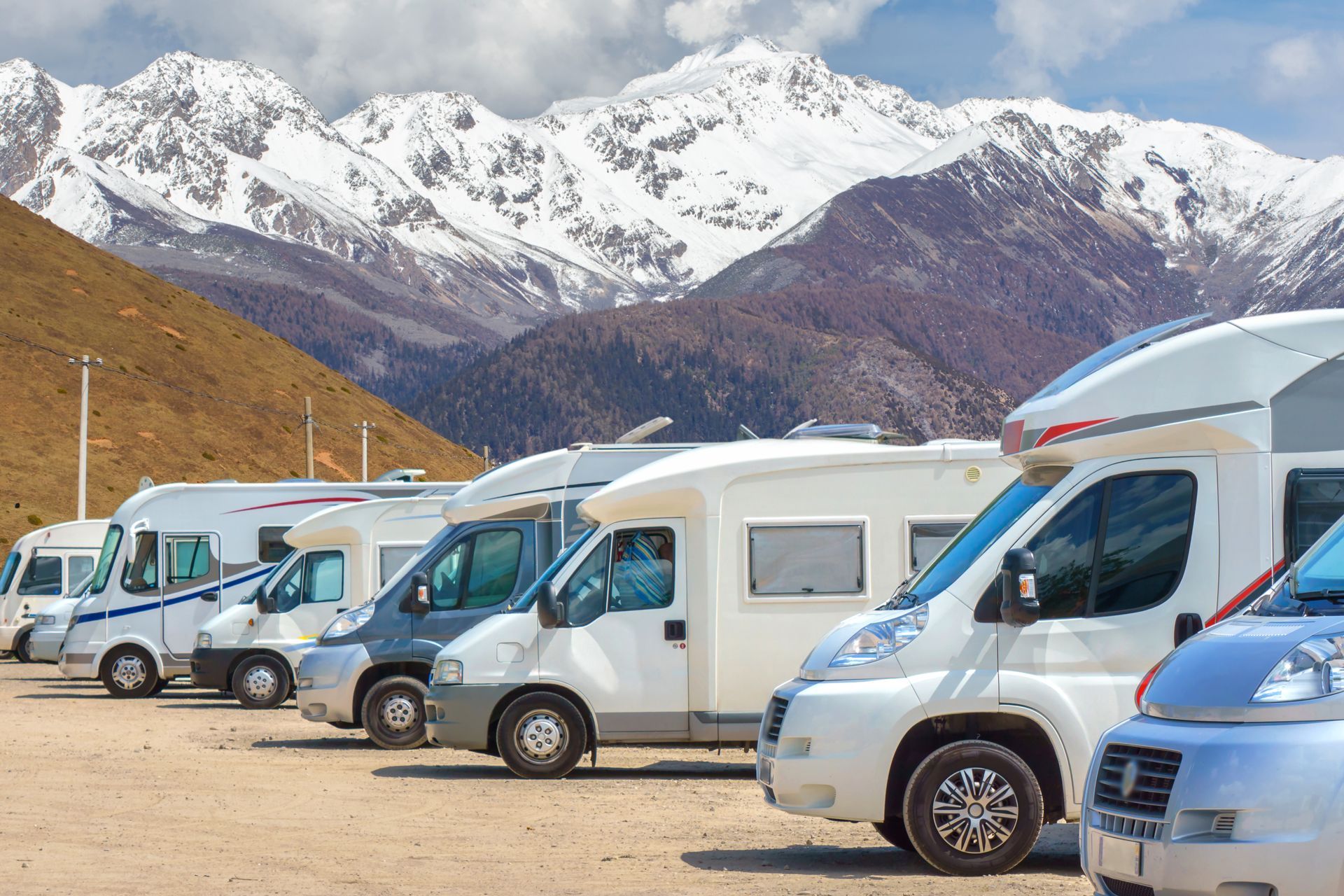 RVs parked in a row on a sunny day with mountains in the background.