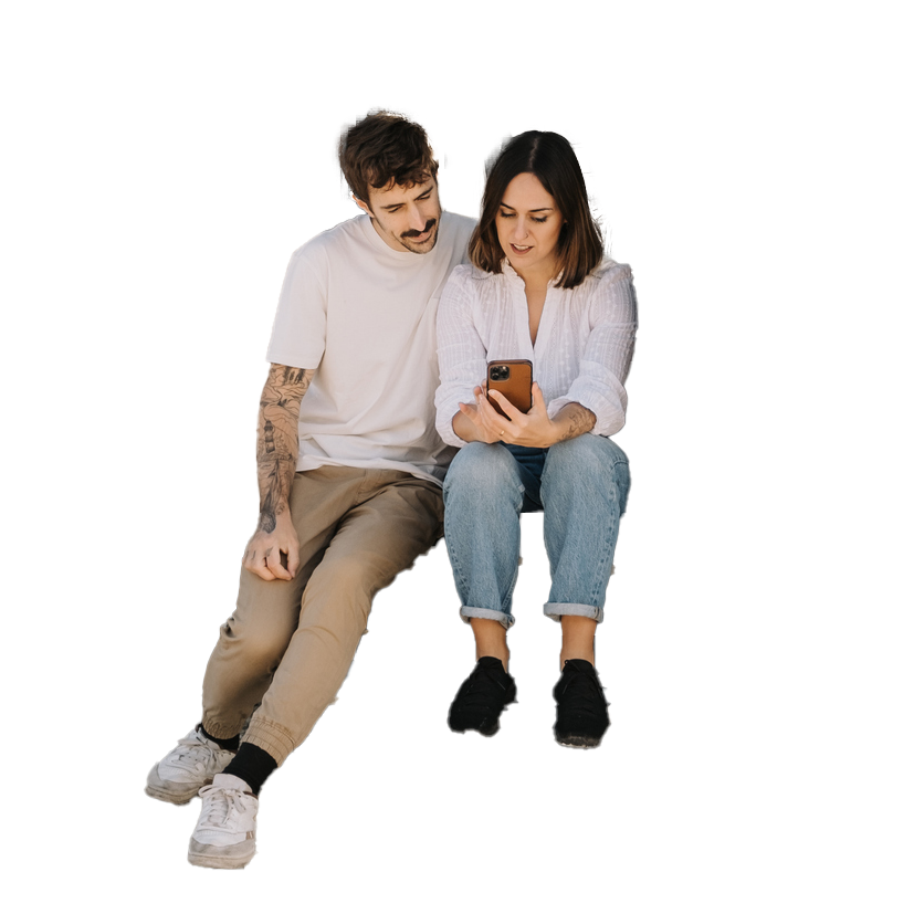 Couple sitting, looking at a phone. Man has tattoos, both are smiling and light-skinned.