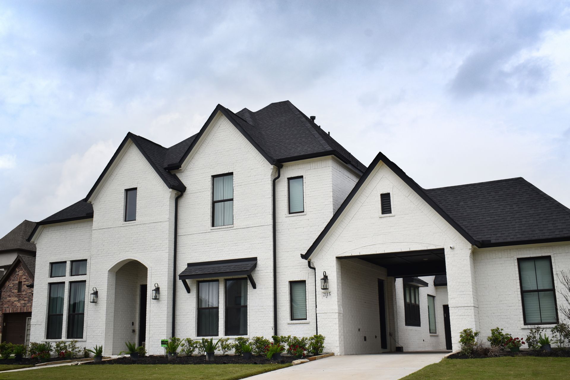 Image of a two story white home with a black roof and a green yard. 