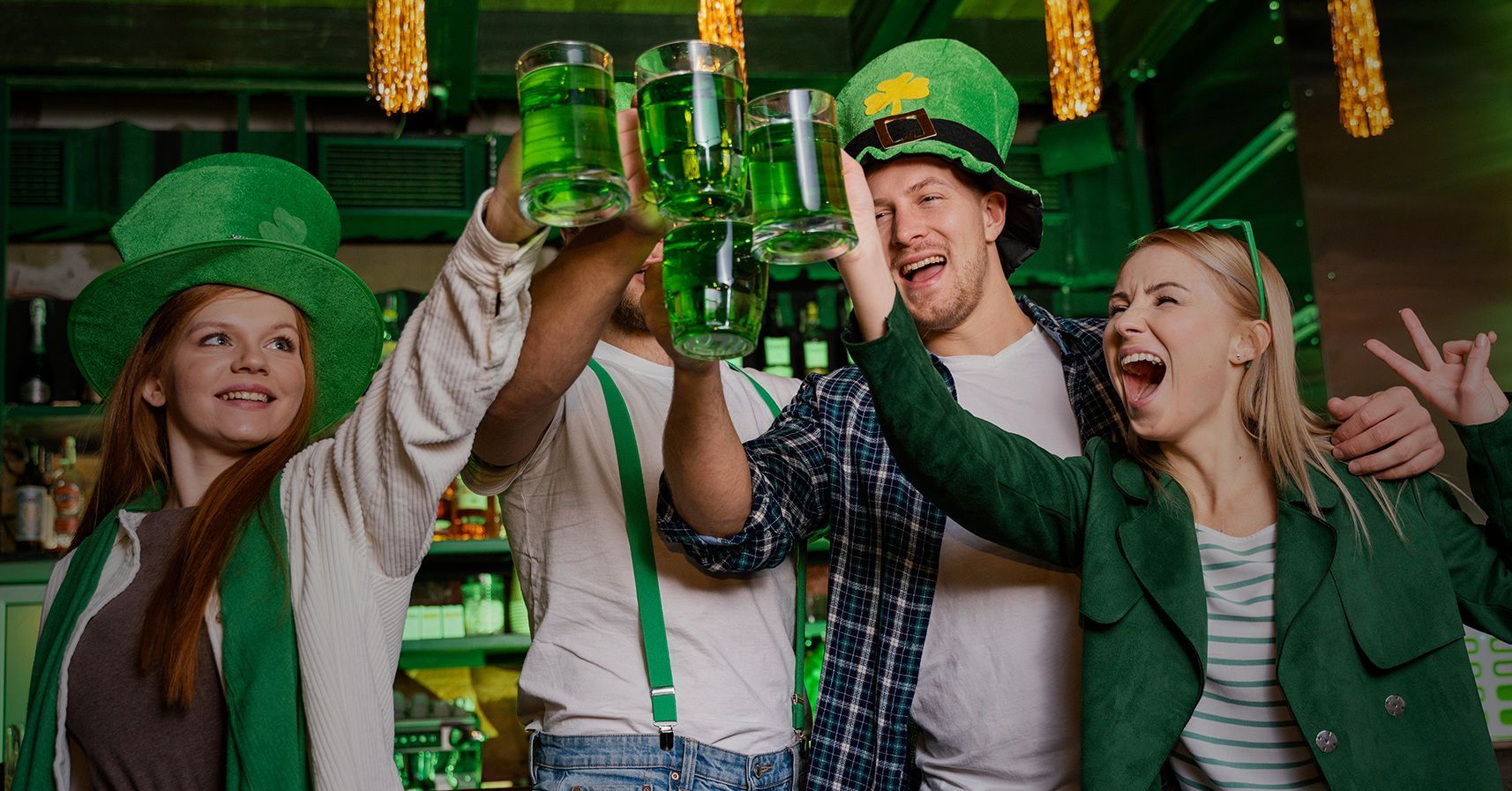 A group of people are toasting with green beer mugs in a bar.