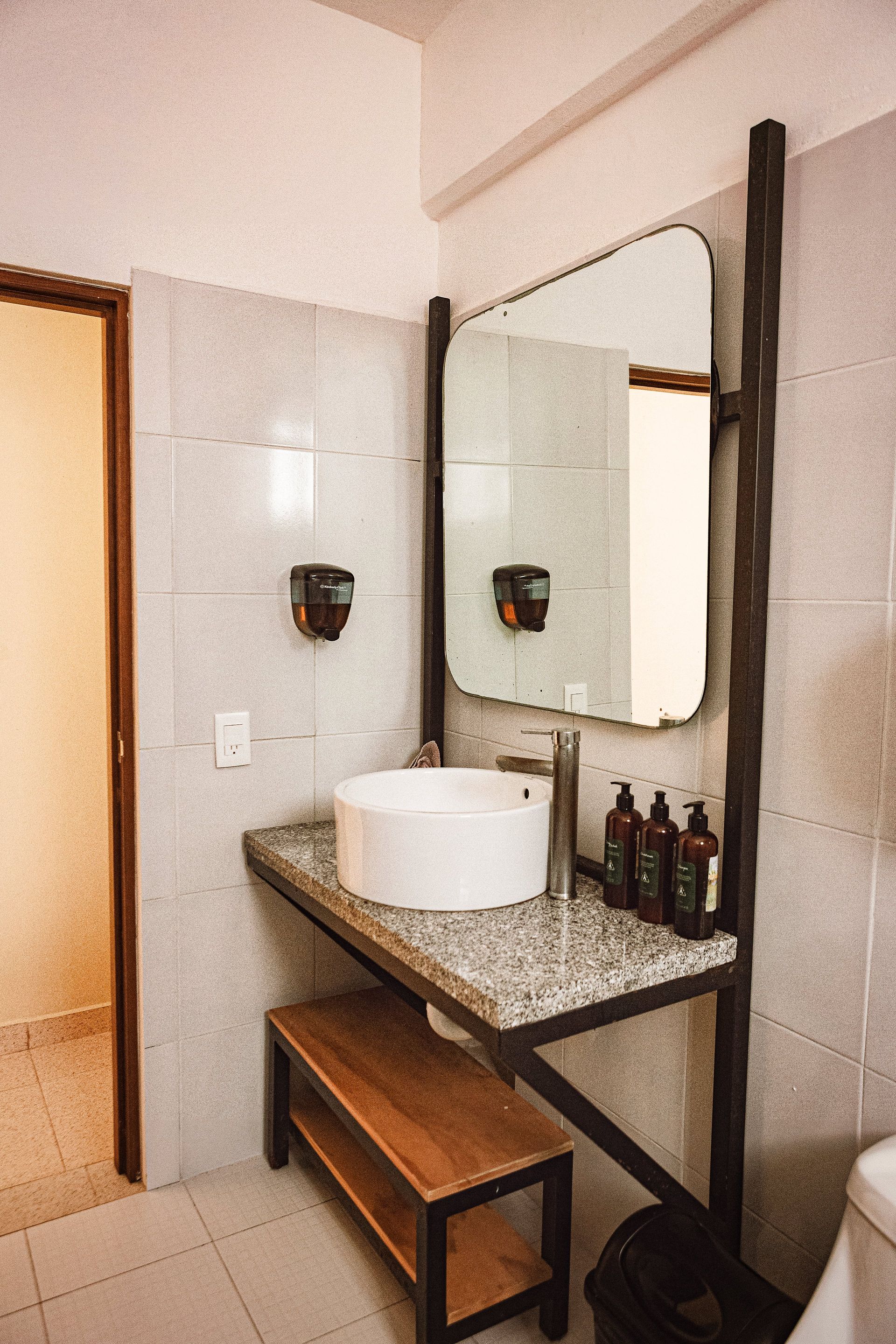 A bathroom with a sink , mirror and soap dispensers