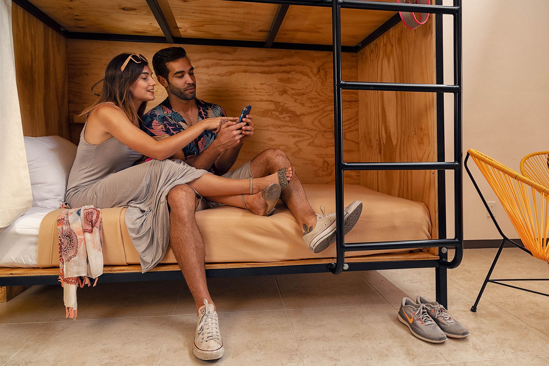 A man and a woman are sitting on a bunk bed looking at their phones.