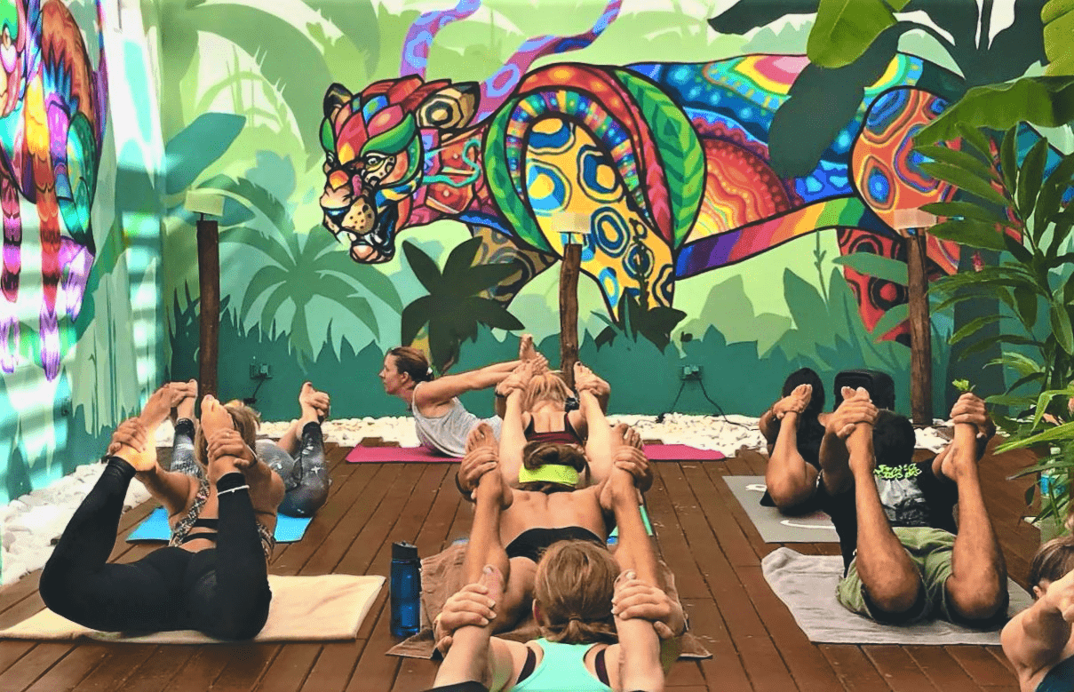 A group of people are doing yoga on a wooden deck in front of a colorful mural.