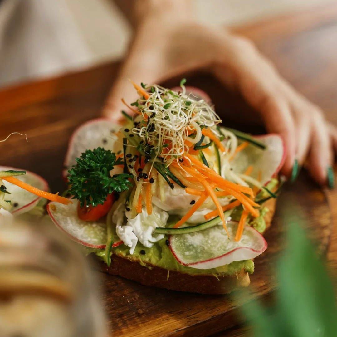 A close up of a person holding a sandwich with vegetables on a wooden table.
