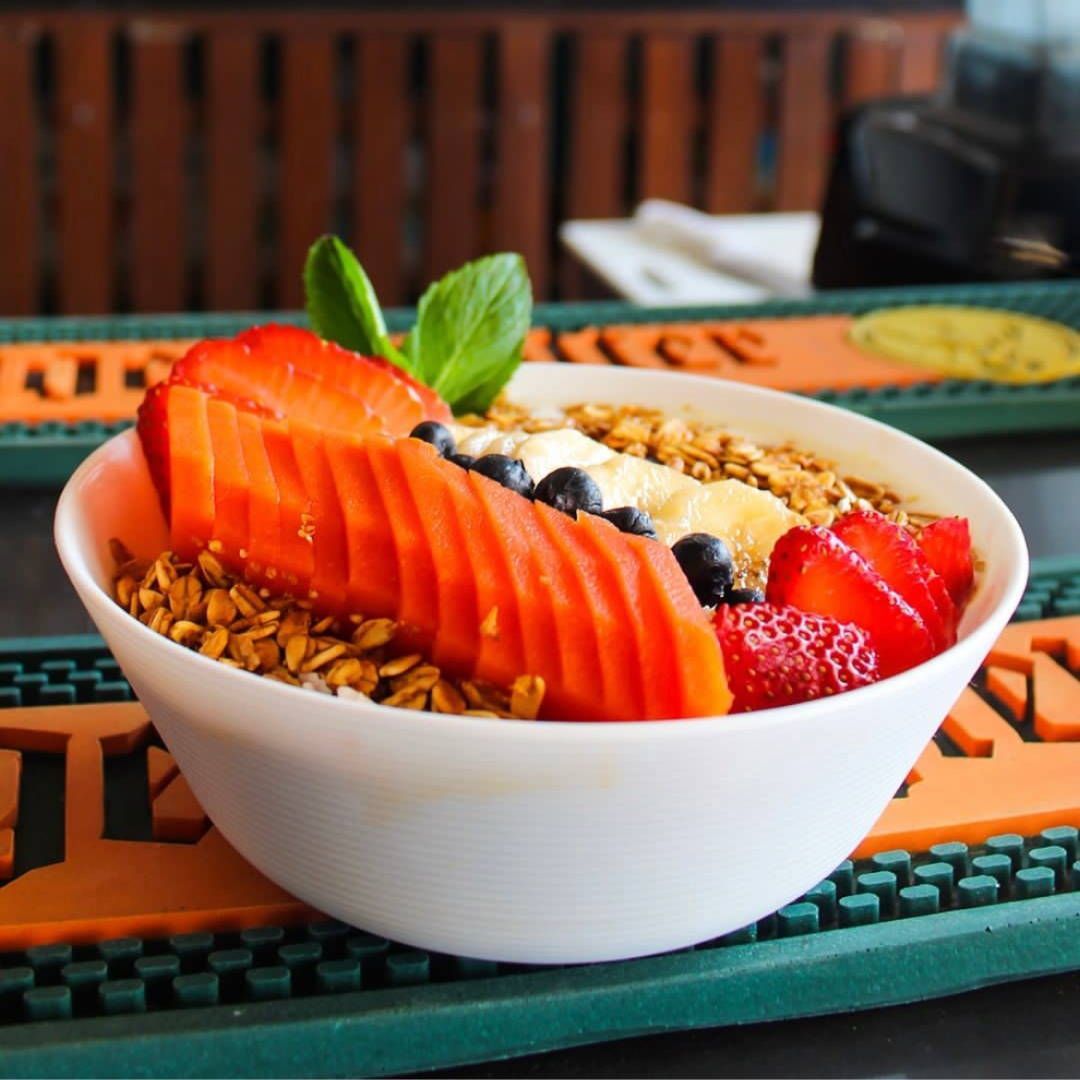 A white bowl filled with granola strawberries and blueberries