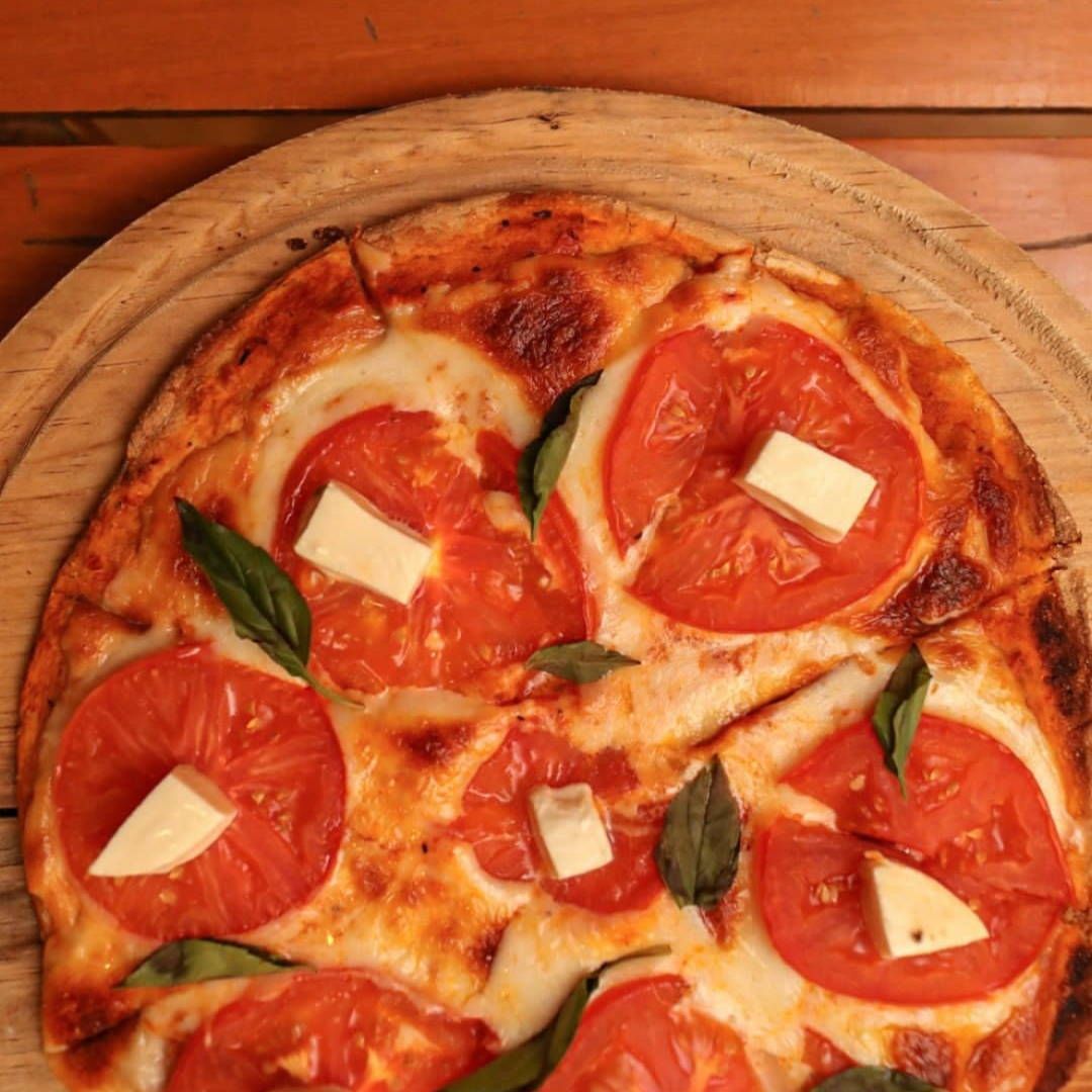 A pizza with tomatoes and cheese on a wooden cutting board