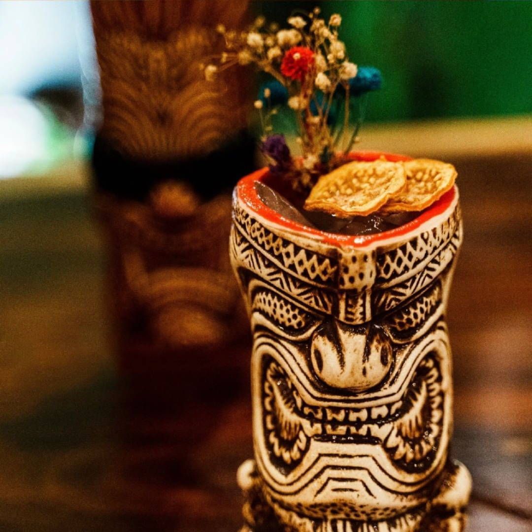 A tiki statue with a drink in it is on a table.