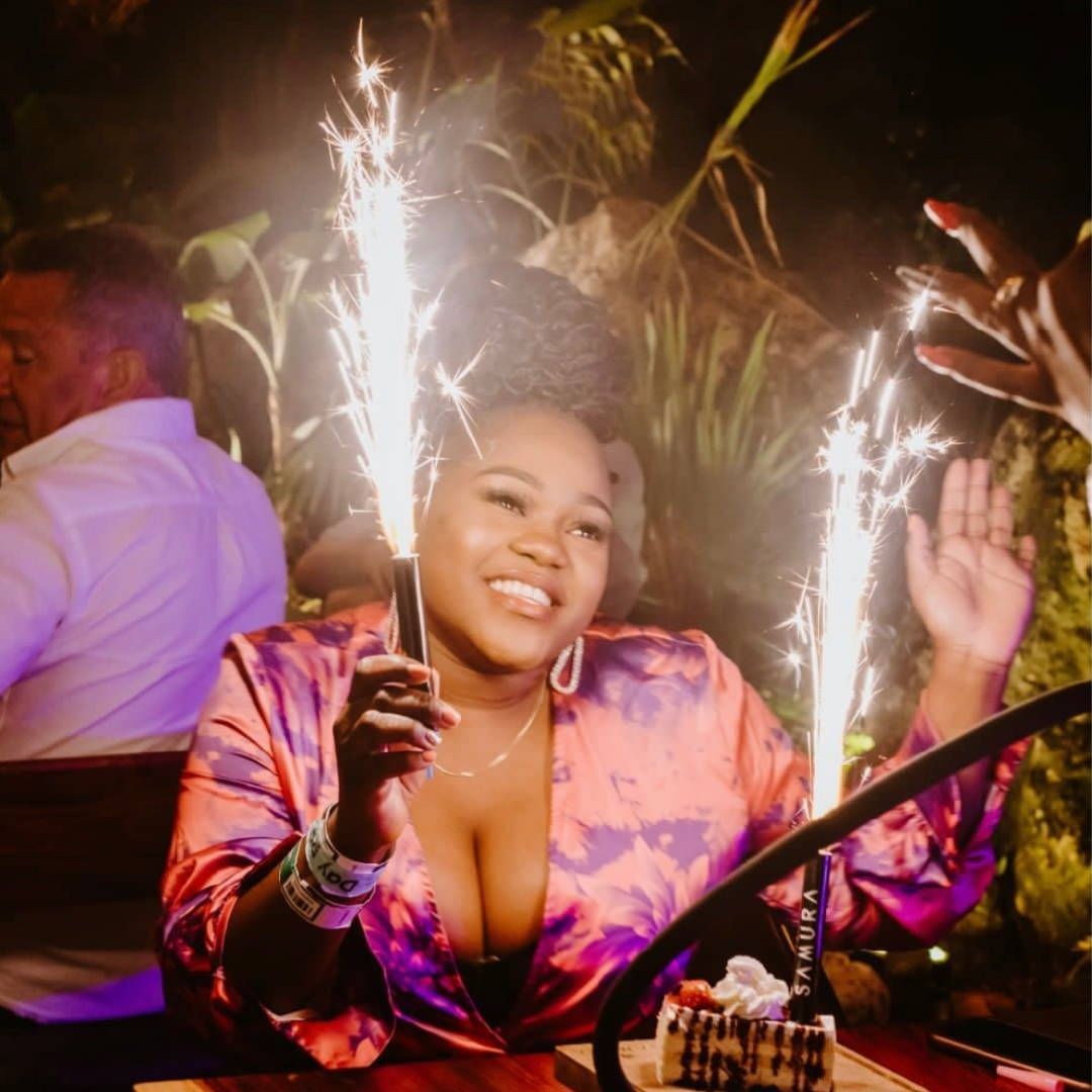 A woman is sitting at a table holding two sparklers.