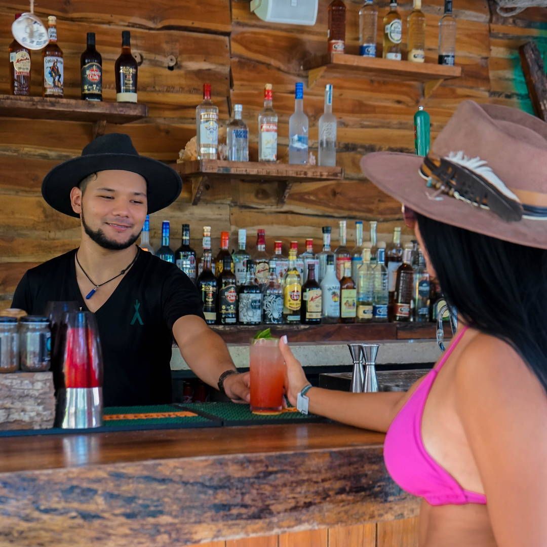 A man in a hat is serving a drink to a woman in a bikini