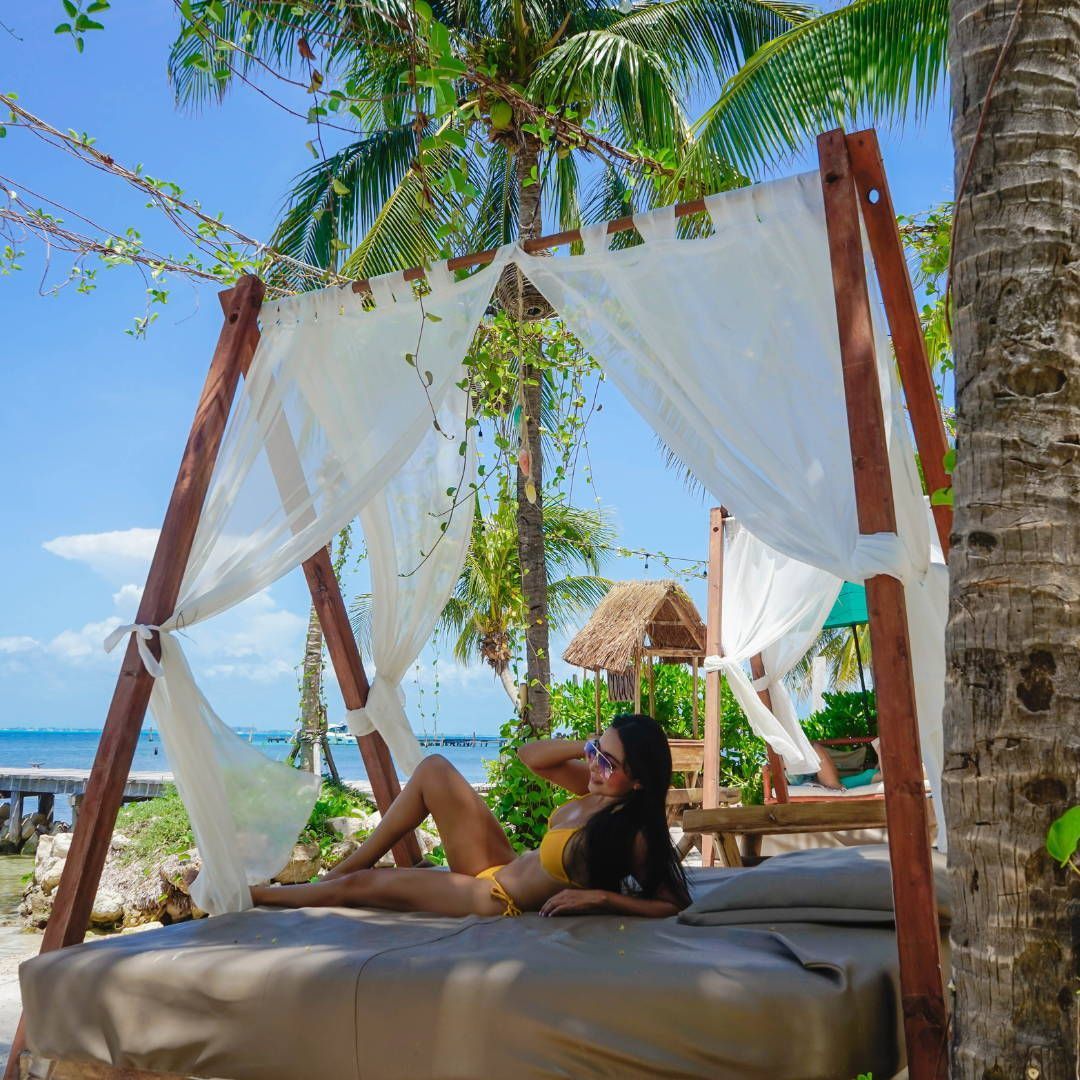 A woman in a bikini is laying under a canopy bed on the beach.