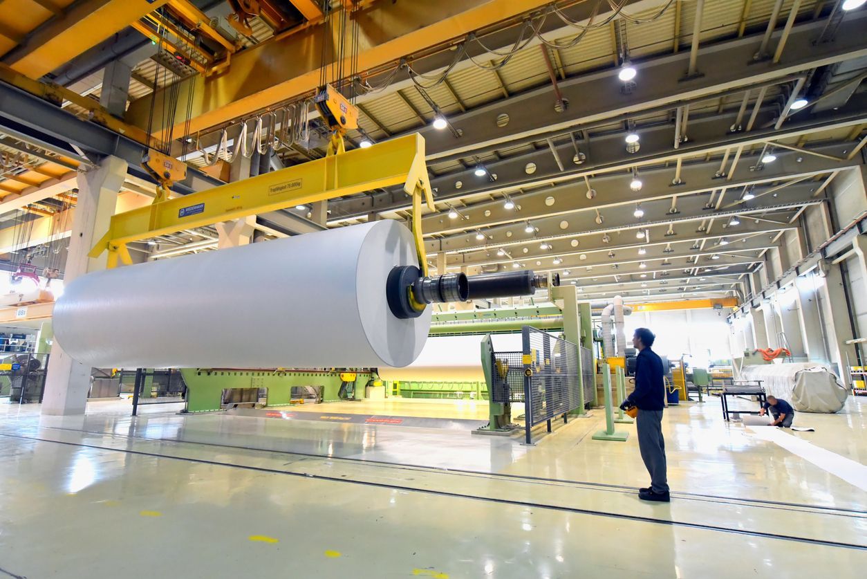 A man is standing in front of a large roll of paper in a factory.