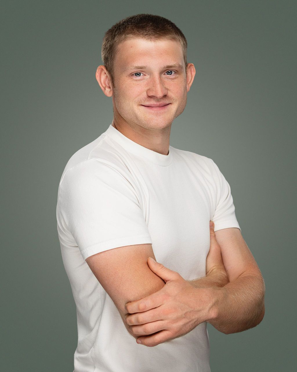 Man in white t-shirt, arms crossed, smiling. Set against a gray background.