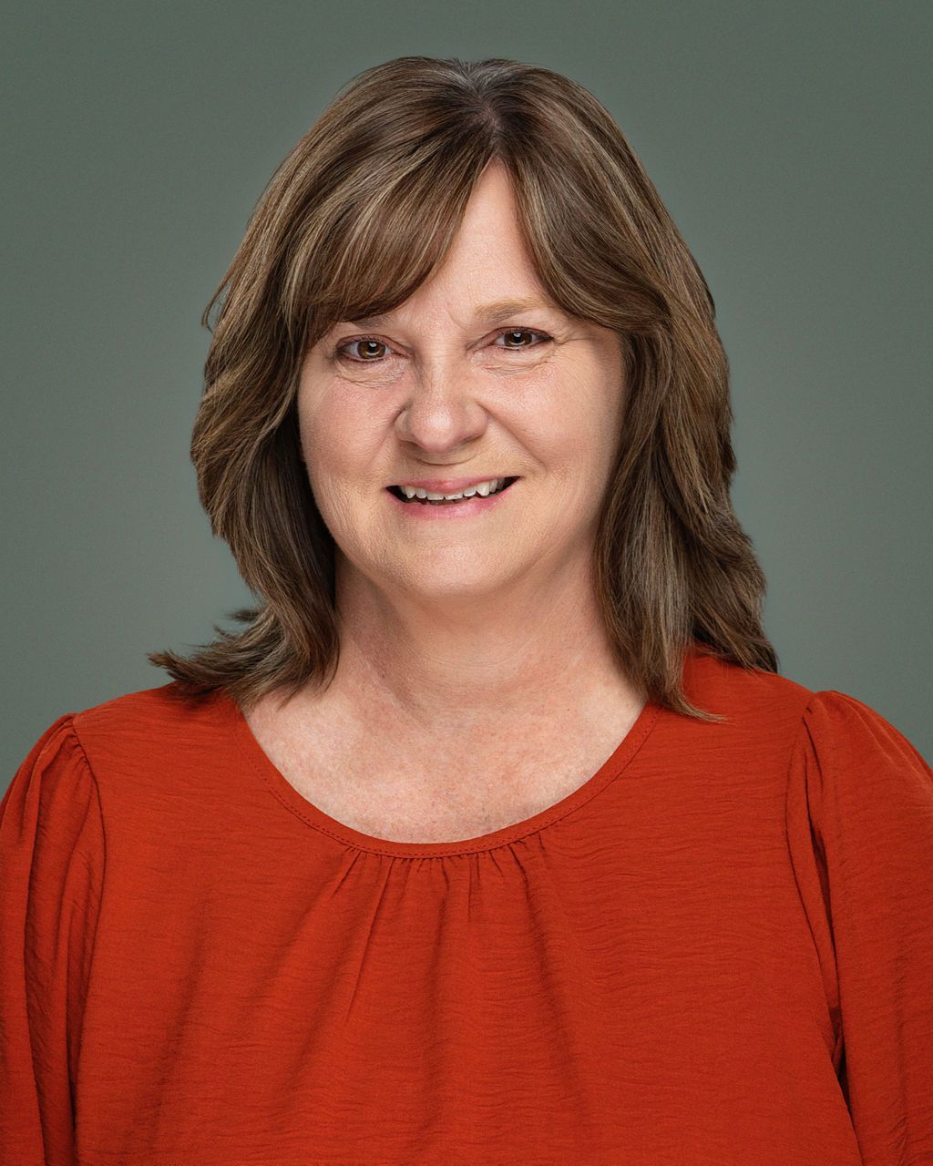 Woman with shoulder-length brown hair, smiling, wearing a red top against a green background.