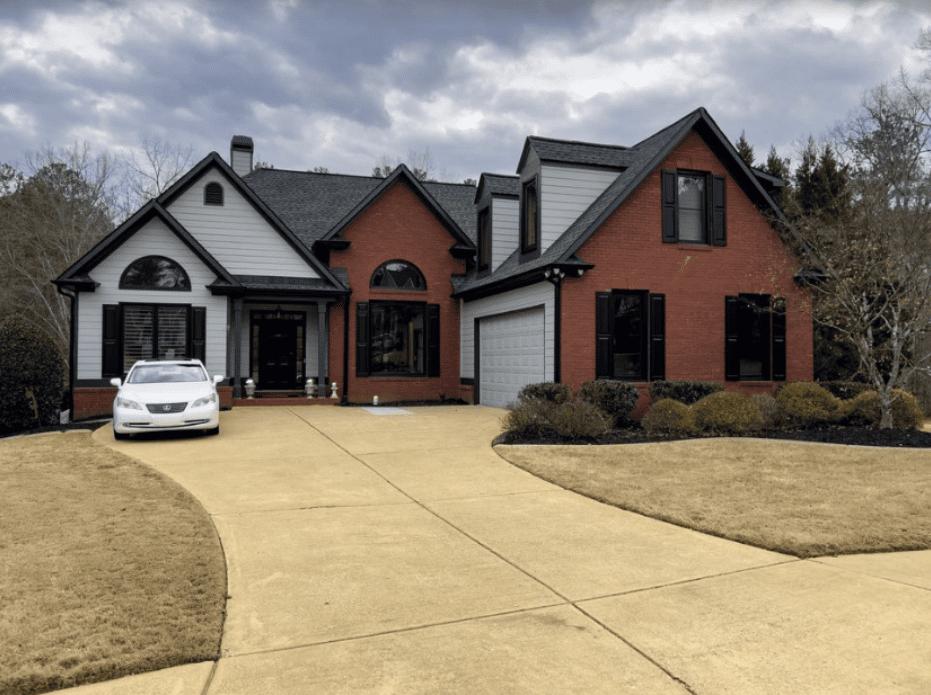 A white car is parked in front of a large brick house.