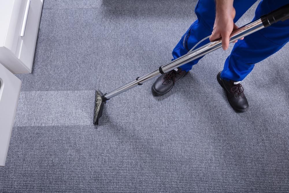 A Man is Cleaning a Carpet With a Vacuum Cleaner — Encore Carpet Professionals in Elanora, QLD