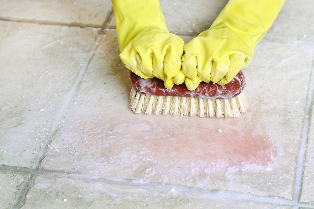 A Person Wearing Yellow Gloves Is Cleaning A Tile Floor With A Brush — Encore Carpet Professionals in Parkwood, QLD