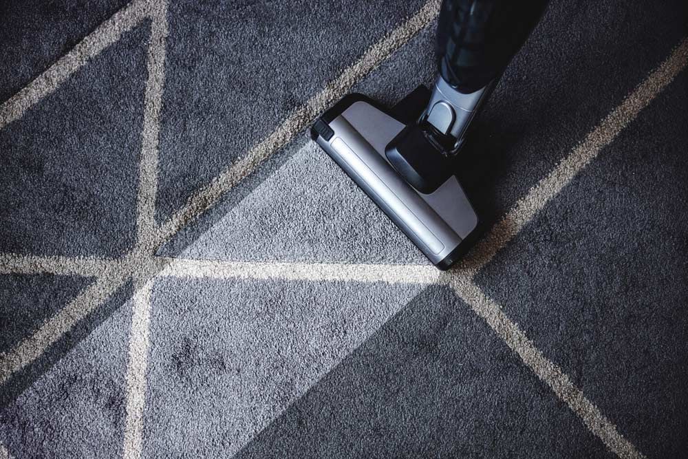 A Person Is Using A Vacuum Cleaner To Clean A Carpet — Encore Carpet Professionals in Parkwood, QLD