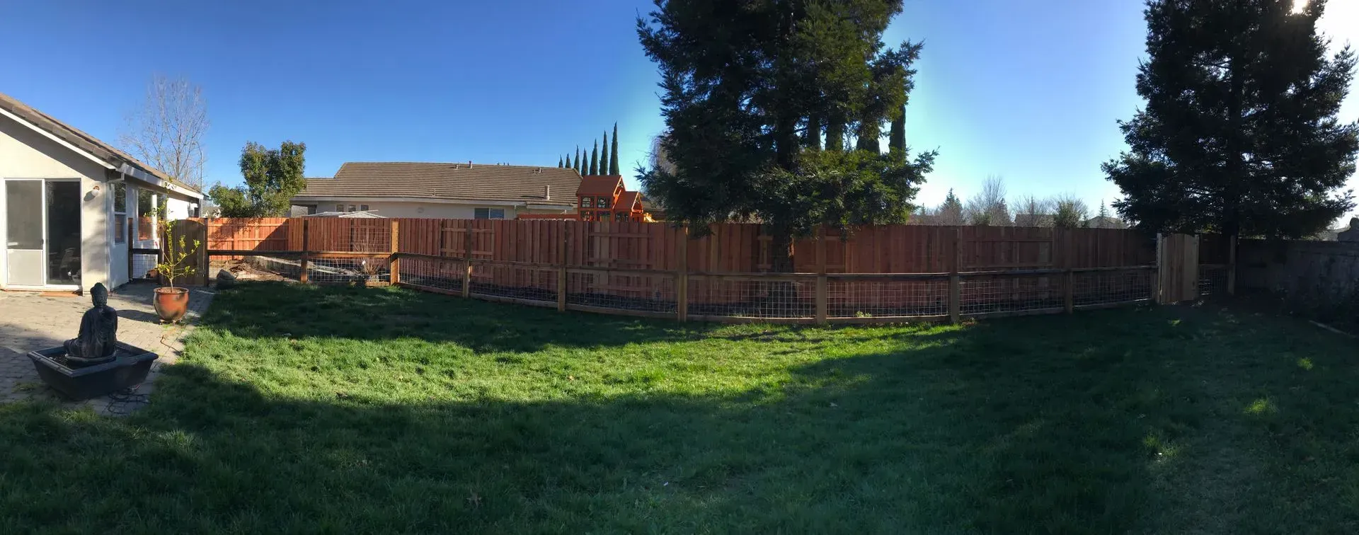 Backyard with green grass, brown fence, and a clear blue sky.