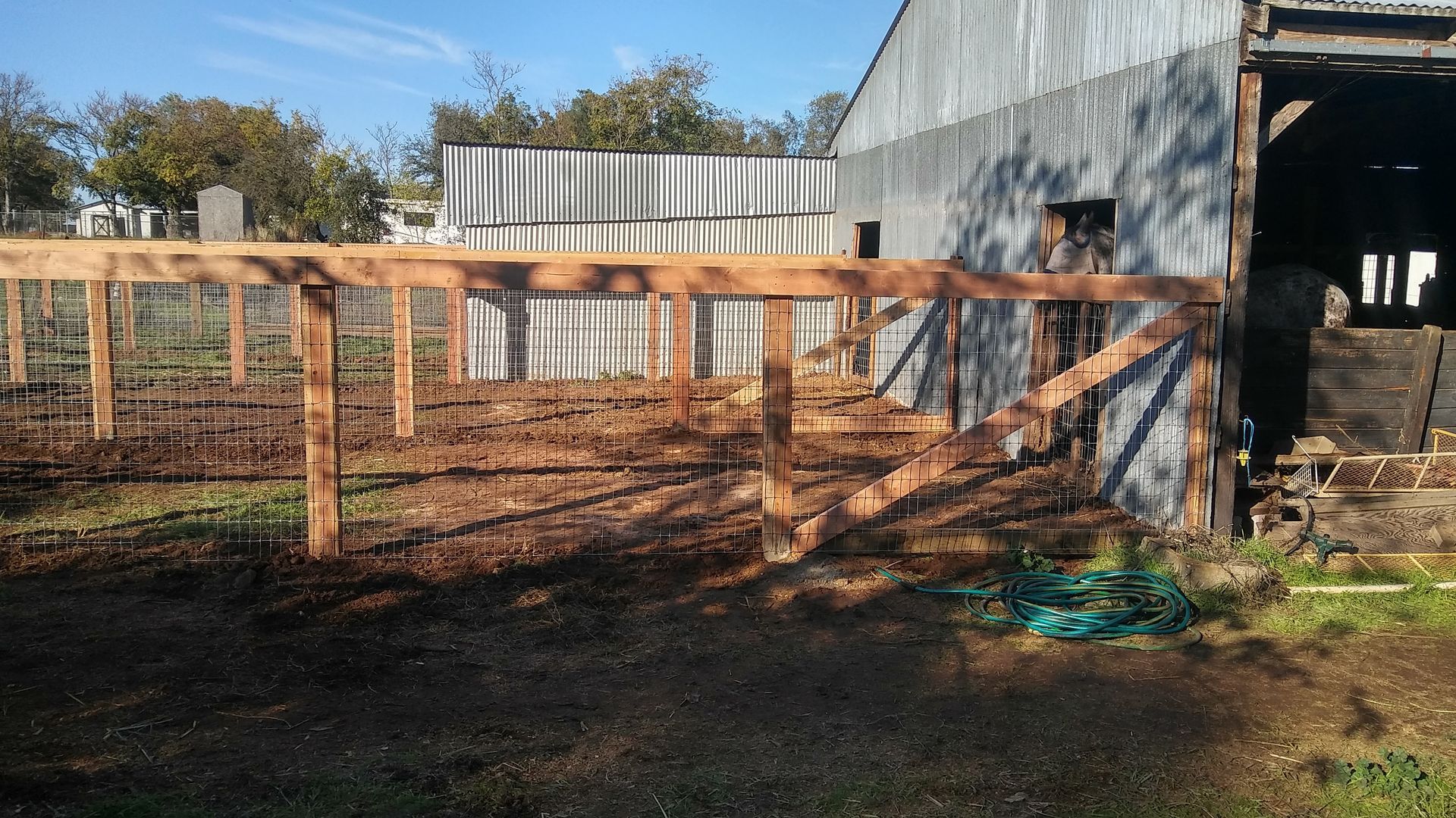Wooden fence with an open gate next to a house's exterior wall. A concrete walkway leads toward a truck.
