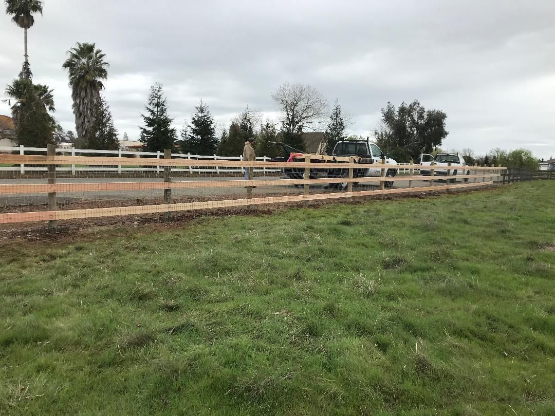 Residential driveway with wooden retaining wall and fence, cars, and a house. Concrete pavement.