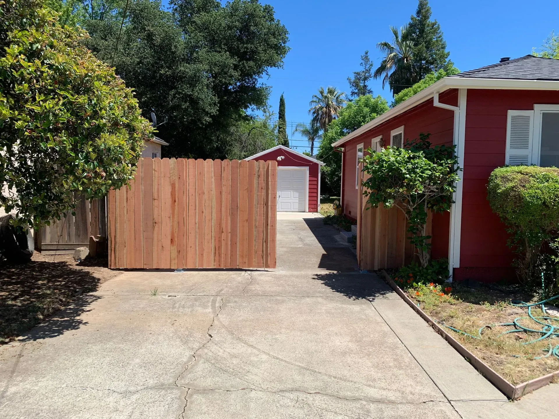 Driveway with a wooden fence, red house, and white garage on a sunny day.
