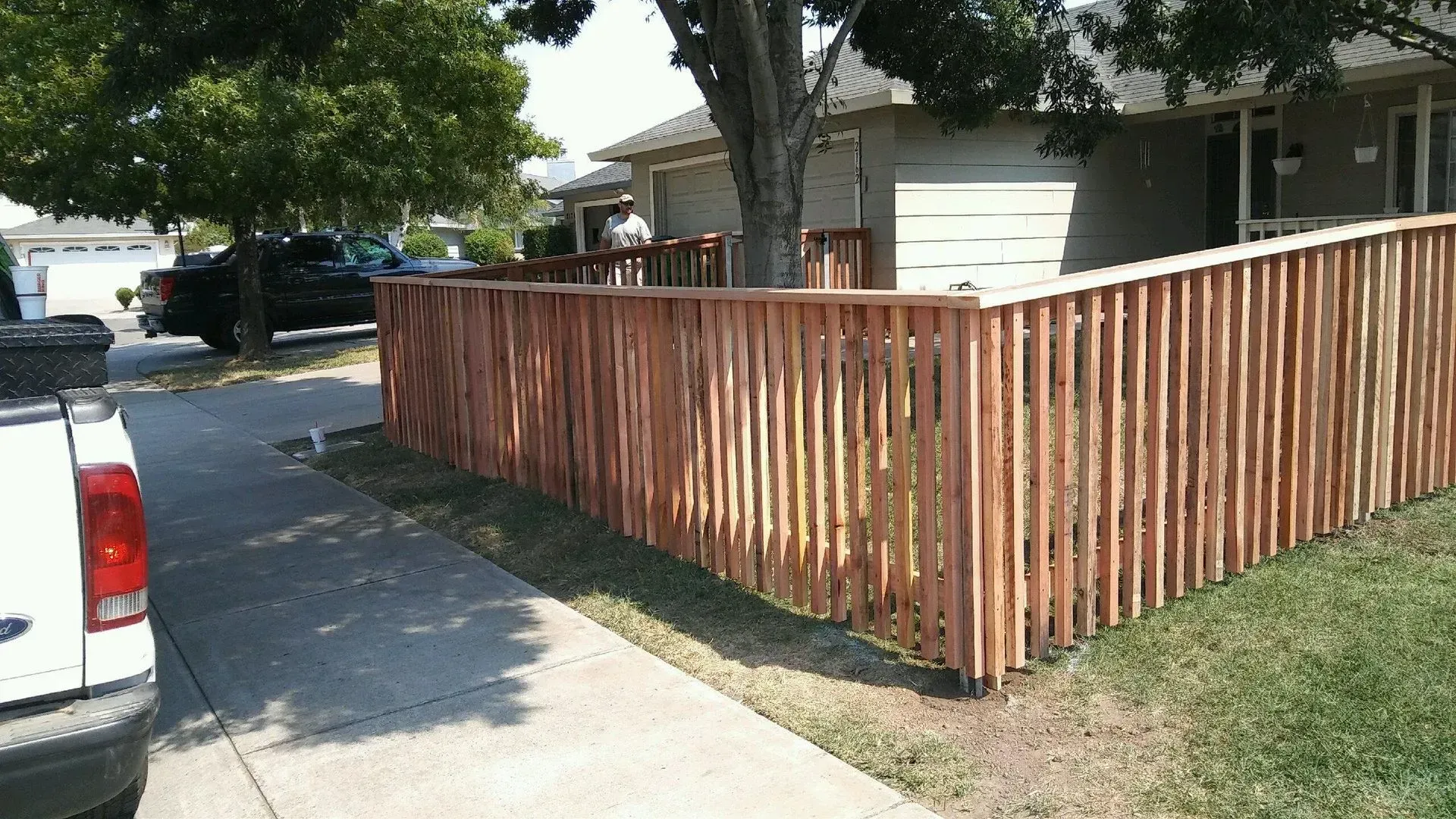 Wooden fence in front of a house, curved along a driveway and grass lawn.