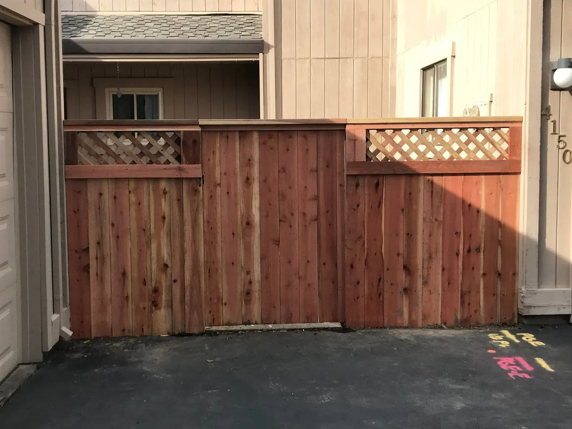 Wooden fence in front of a beige building with a small window and a lamp.