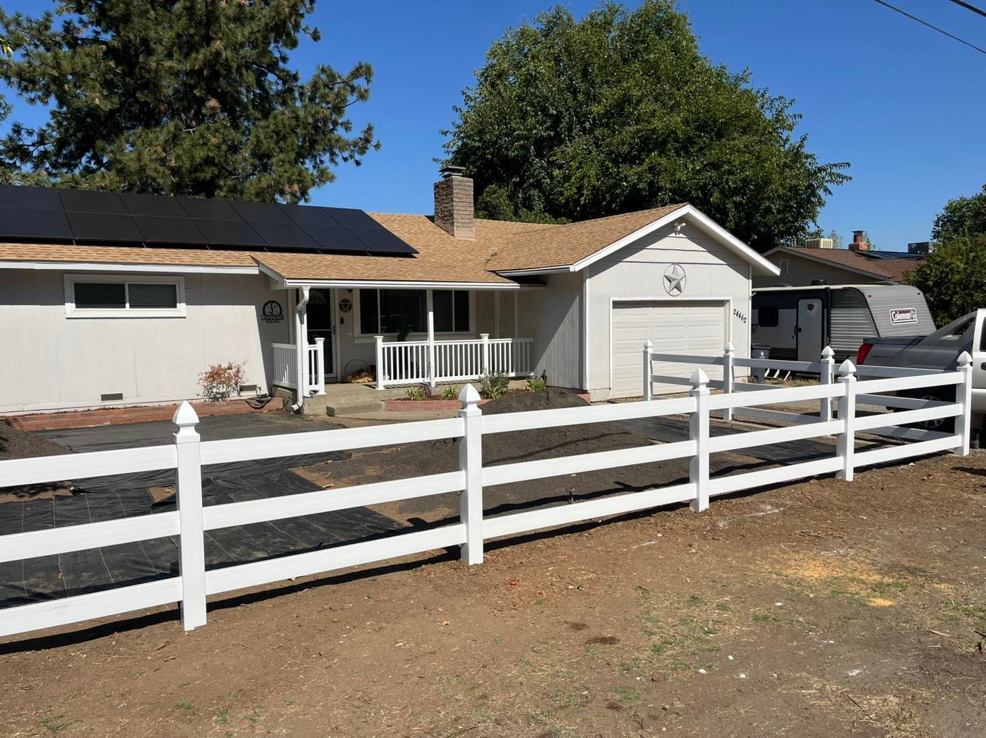 White house with a white fence, solar panels, and a blue sky.