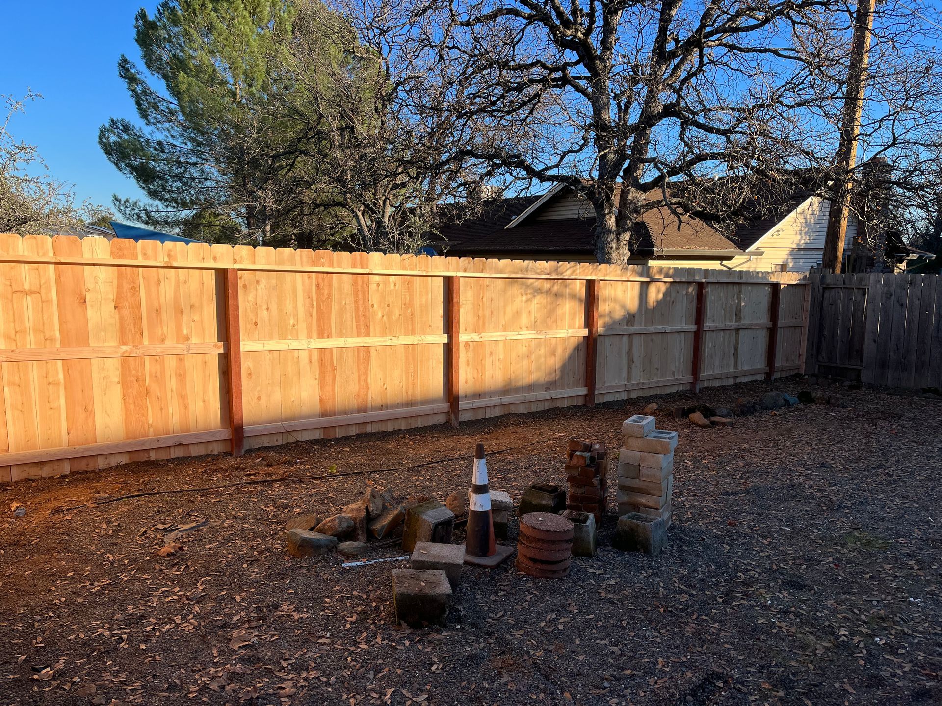 Wooden fence with black metal gate, built next to a gravel-covered yard.