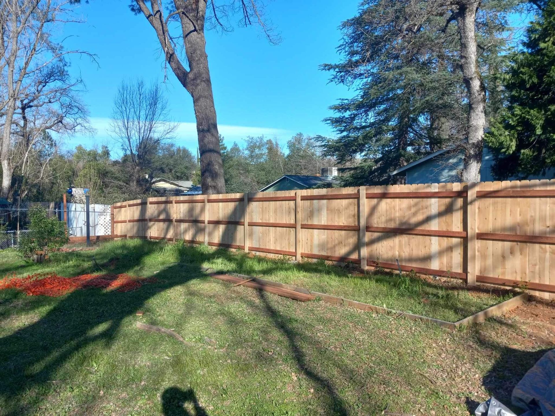 Wooden fence in a backyard with a tree and green grass under a clear blue sky.