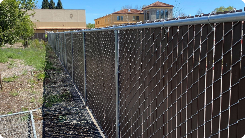 Wooden and wire fence with gate in backyard, trees and sunlight.