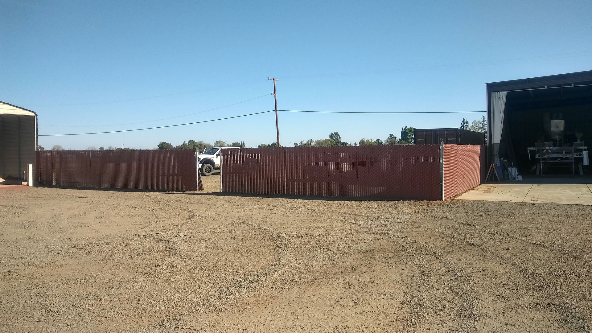Wooden and wire fence with gate in backyard, trees and sunlight.