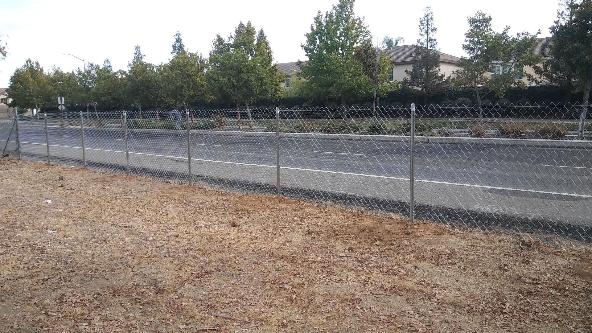 Wooden fence with wire mesh panels, next to a dirt embankment, under trees.